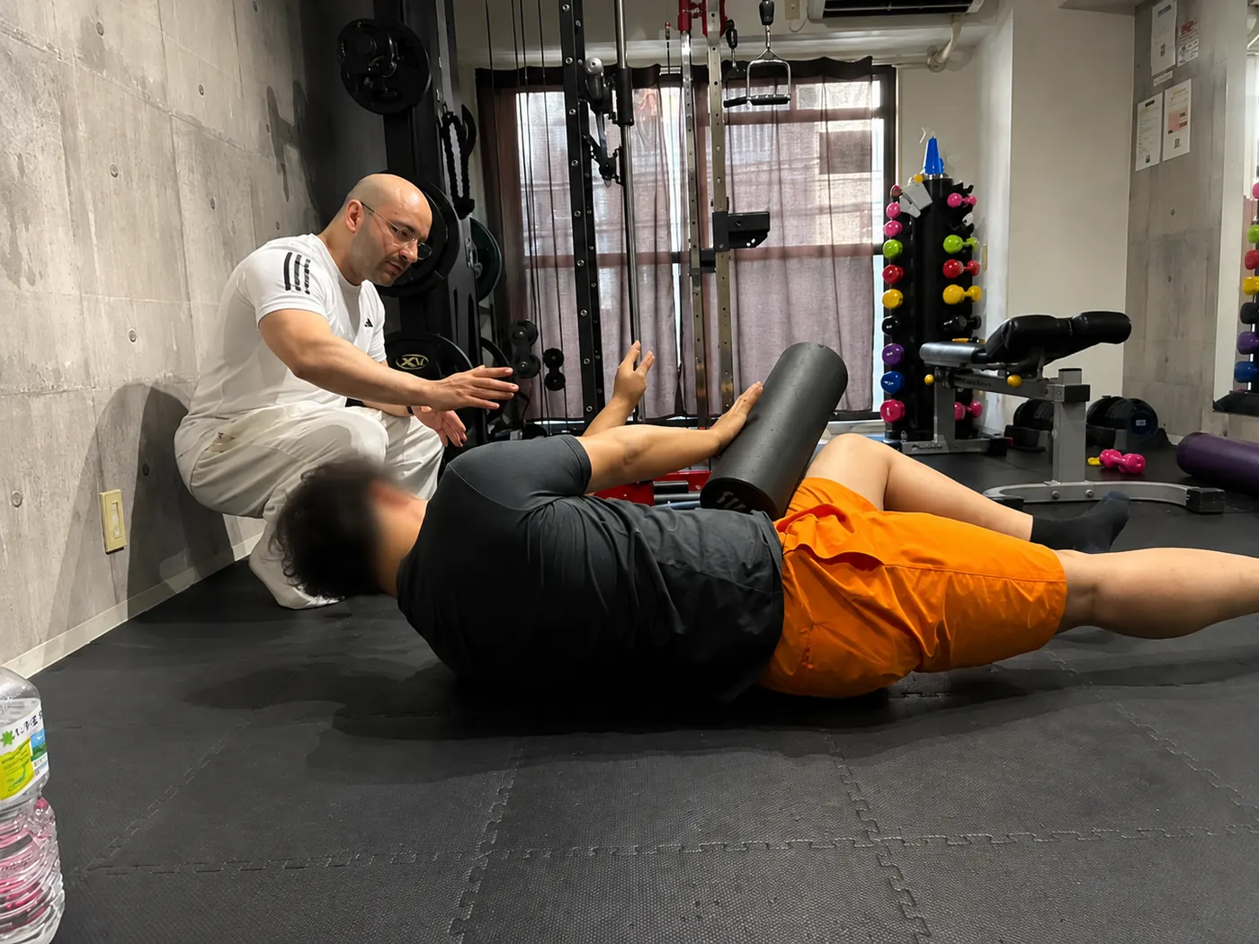Samuel crouches beside a client lying on a foam roller and uses his hands to explain the next movement.
