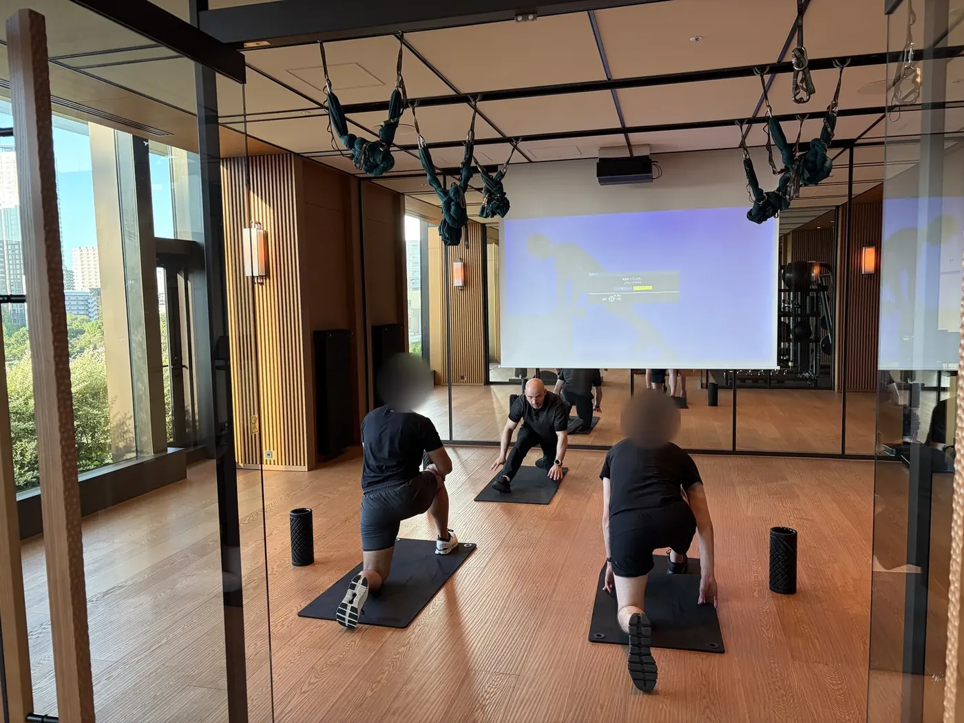 In a bright fitness studio, Samuel demonstrates a half-kneeling mobility warm-up while two clients follow along on mats.